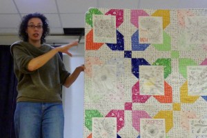 Tamara Kate points to her quilt, being held up by volunteers on stage